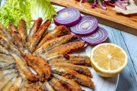 Perinteisiä pescaitos fritos -paistettuja malagalaisia sardelleja sitruunasipulin ja salaatin kera puupöydällä.